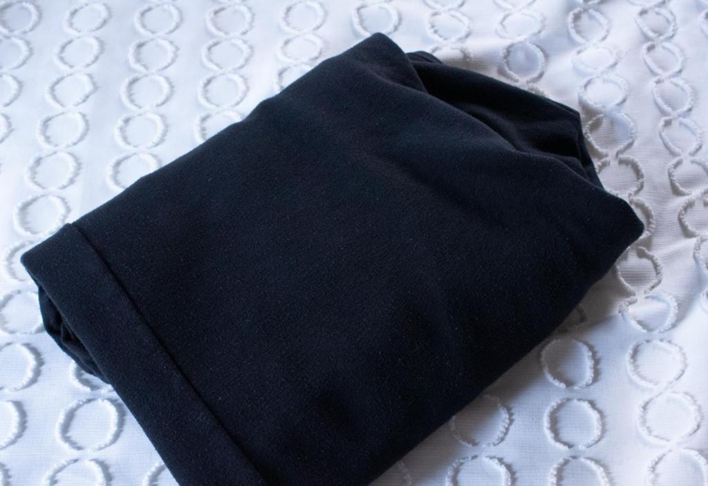 A pair of folder black sweatpants sit on a white comforter on a bed.