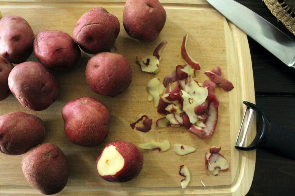 Red potatoes are peeled on a cutting board.