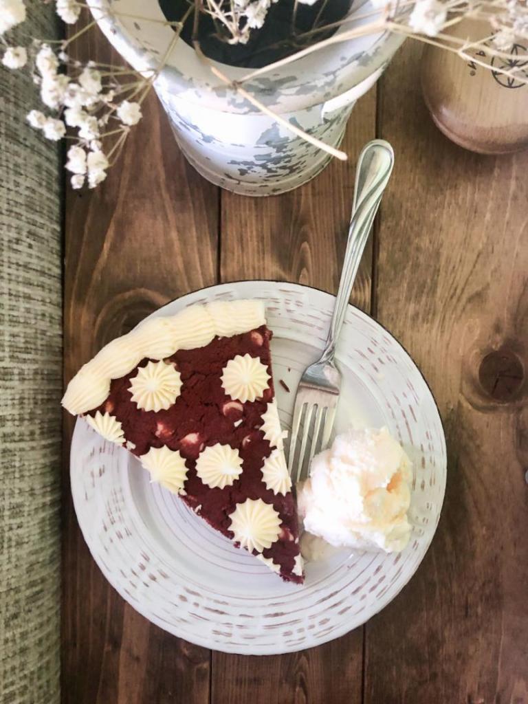 A cookie cake is sliced and served with a scoop of ice cream on a rustic table.