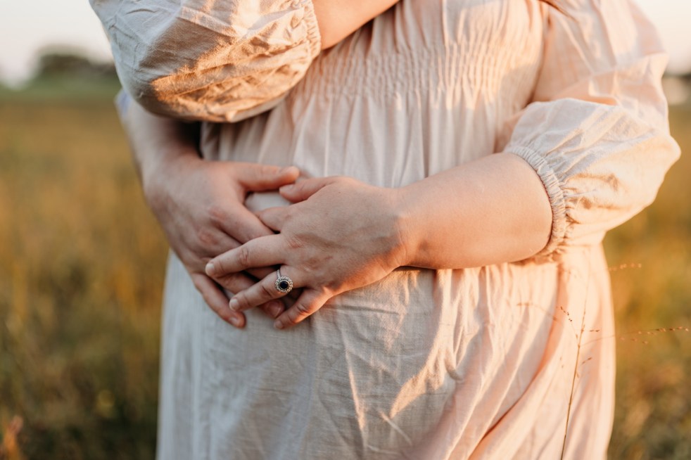 A man wraps his arms around a pregnant woman caressing her belly.