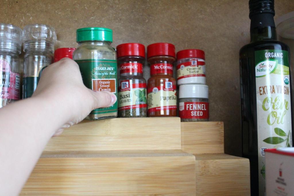 Spices in mismatched jars are being removed from a shelf for spice rack organization.