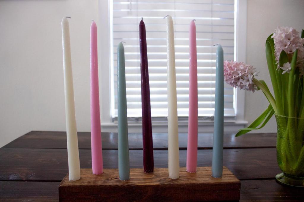 A DIY rustic wood candle holder is set up on a table near flowers.