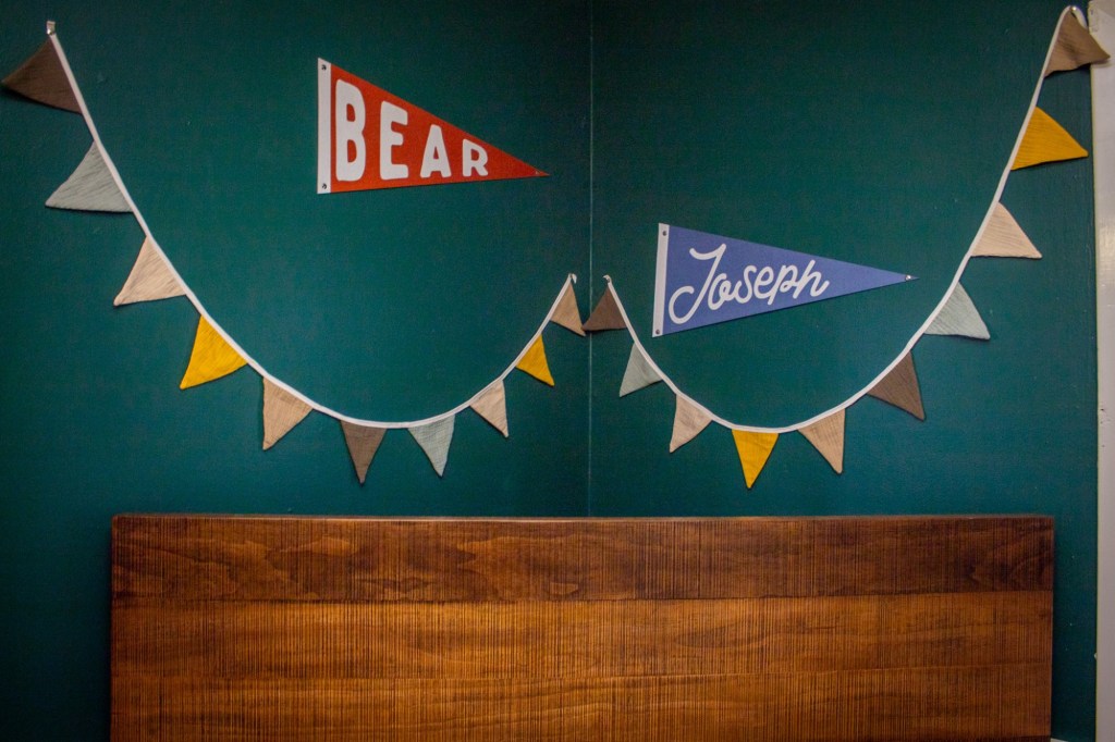 Pennants read Bear Joseph across them and hang behind a crib.