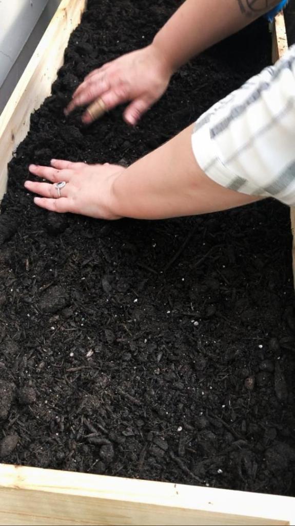 A woman pats down soil into a garden bed in efforts to learn how to prepare raised beds for winter.
