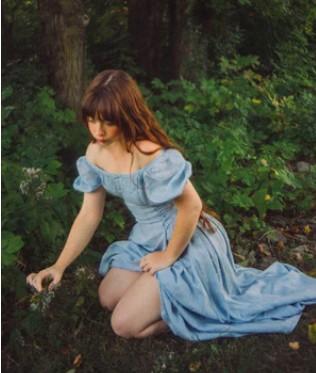 A woman wears a blue dress in the forest.
