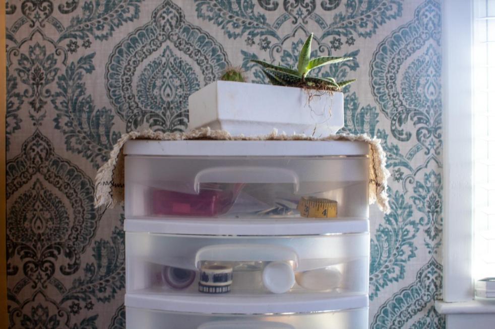 Craft drawer organization is done with a tower of plastic drawers with a plant placed on top for fun.
