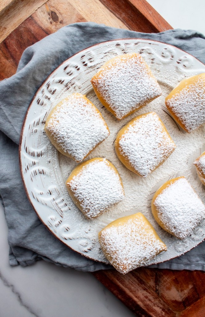 Baked beignets are plated over a wooden serving tray.