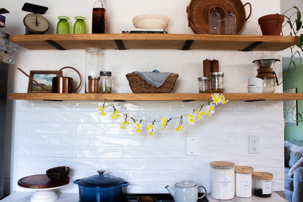 A DIY daffodil garland is strung on an open shelf above a stove.