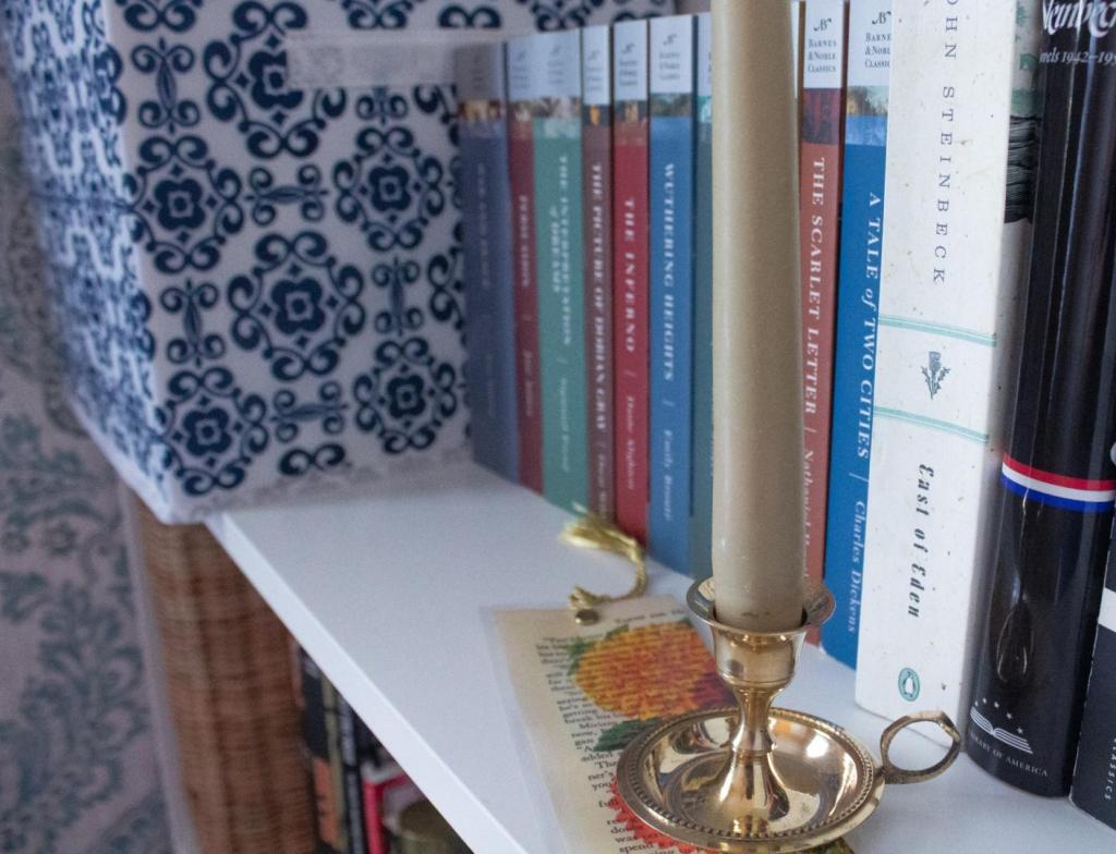 Bookcase styling is done easily with a collection of classic novels with pastel paperback covers and a vintage candle holder nearby.